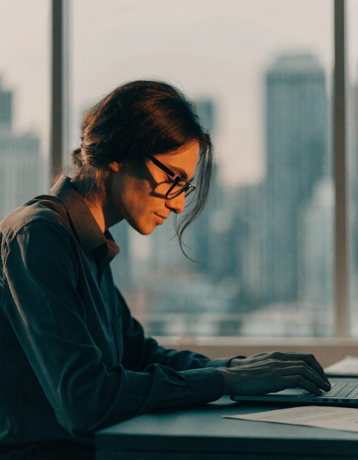 A focused professional at a desk by a window overlooking the city.
