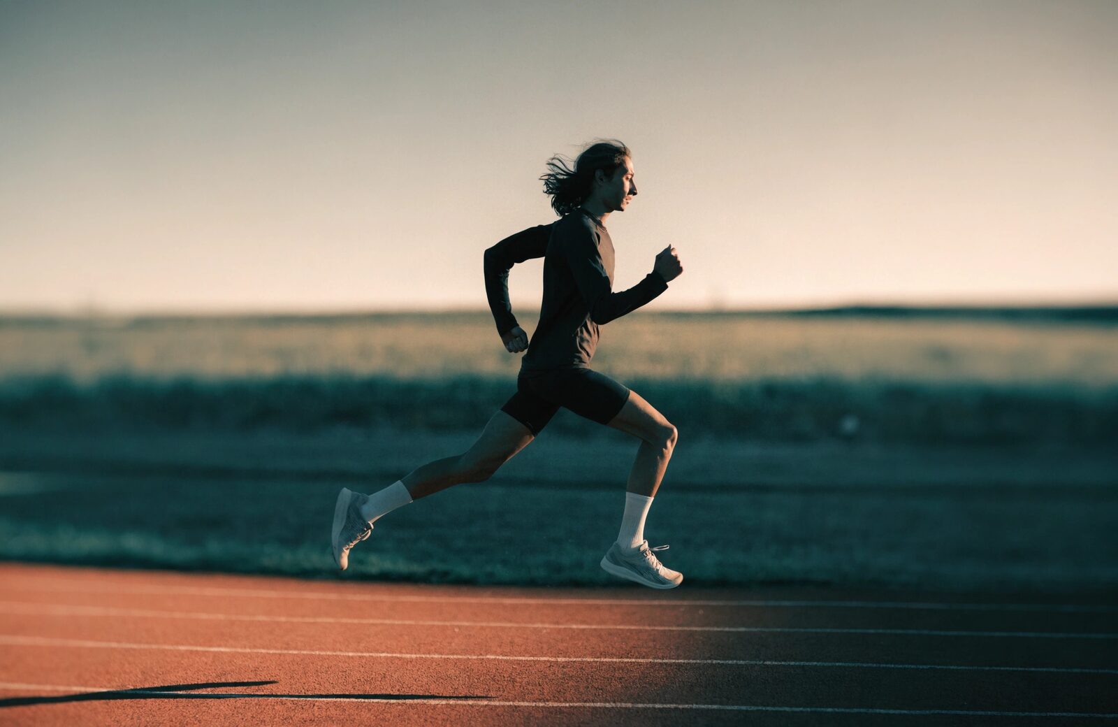 A runner mid-stride on a track at first light.