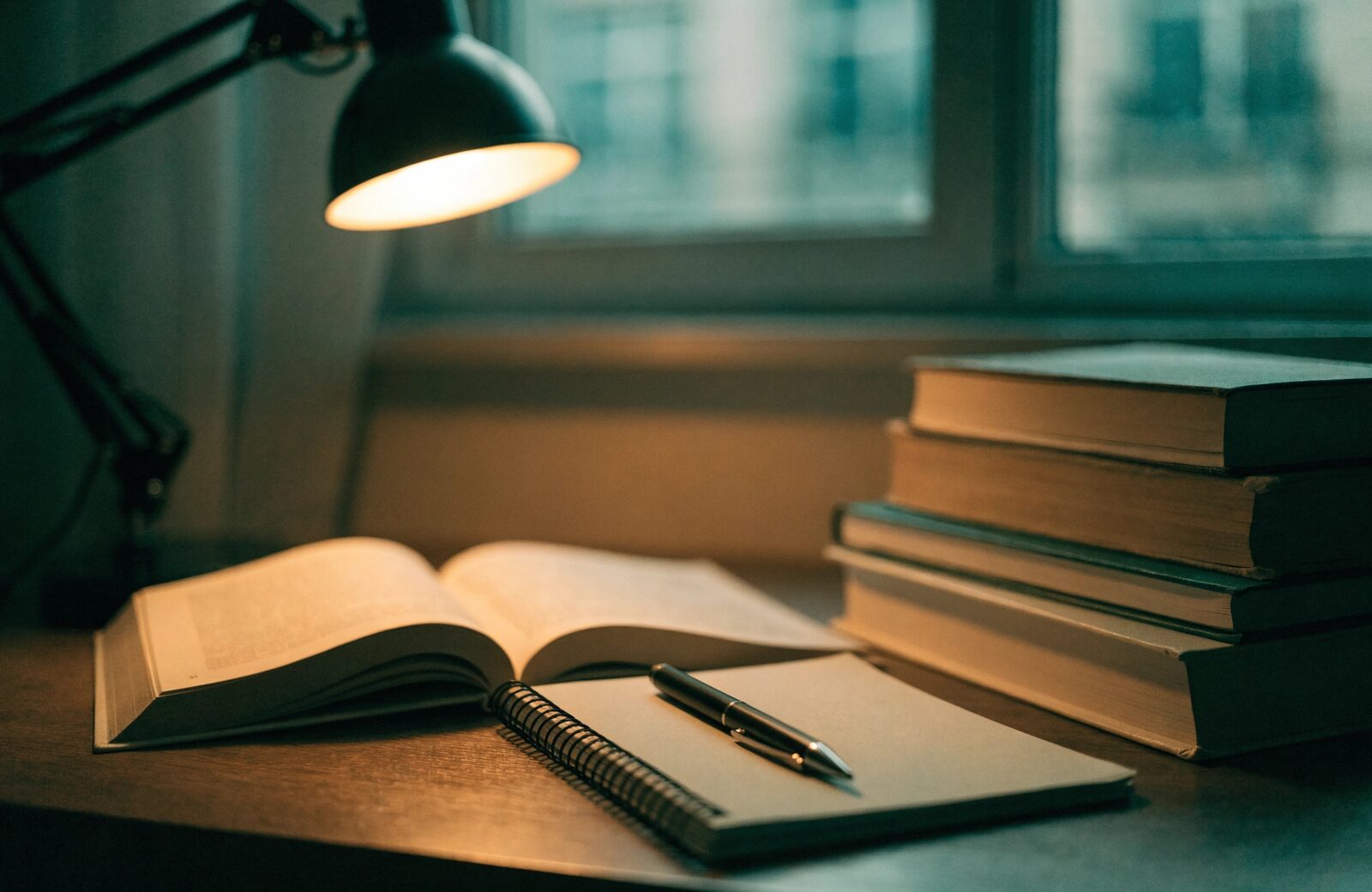 An open book and stacked textbooks under a warm desk lamp.