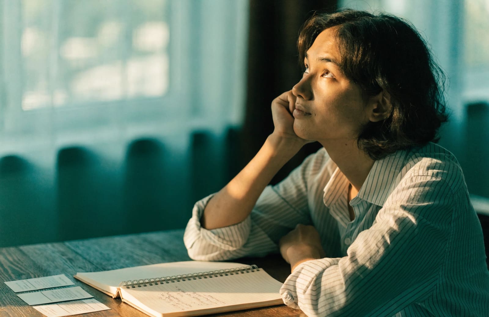 A young adult pausing in quiet recall while studying, warm light, cool shadows.